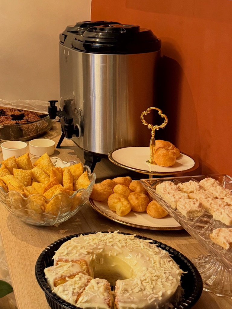 Mesa de coffee break com garrafa térmica de café, bolo, carolinas, pasteizinhos e doces