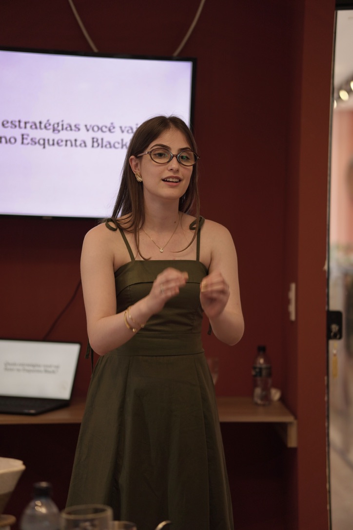 Ana palestrando em frente a uma tela em uma edição do Café com Estratégia